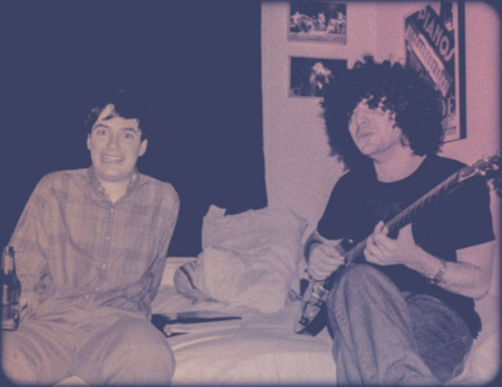 Two friends on a bed, one playing guitar for the other